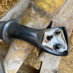 Close-up of a black cordless drill with a damaged battery pack, resting on a weathered surface with straw nearby.