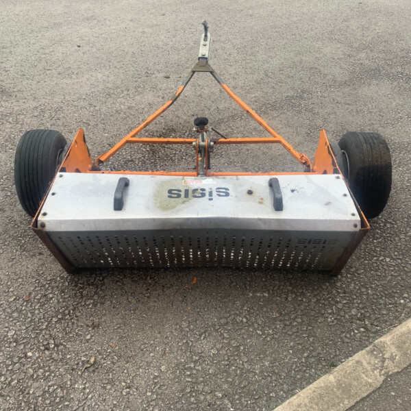Top-down view of an orange metal trailer frame with two large black wheels on a paved surface.