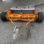 Orange road roller seen from above on asphalt, with large black wheels and metal roller drum; brand name 'SISIS' visible on the machine.