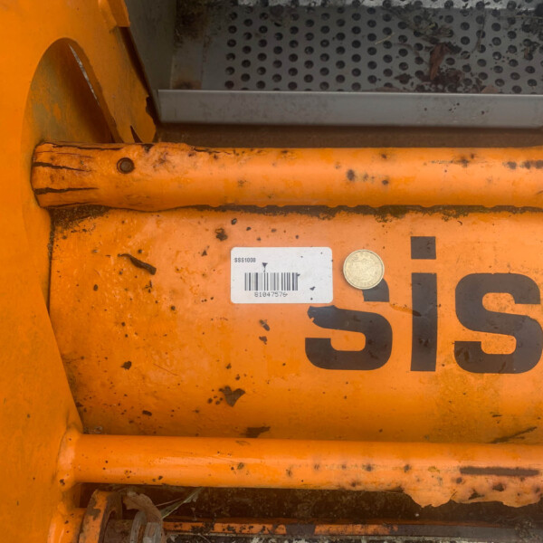 Close-up of orange industrial equipment with a barcode label, dirt, and a coin resting on the surface