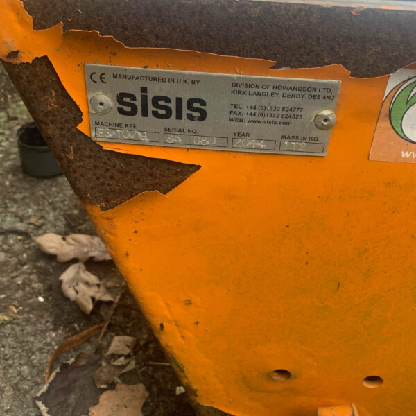 Close-up of an orange, rusted metal surface with a silver nameplate reading 'sisis' and small textual details.