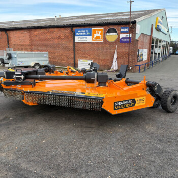 Orange Spearhead Mulcut farming mower in a parking lot in front of a brick building with signs on the wall.