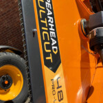 Close-up of an orange heavy-duty construction machine showing a black and yellow warning label, with a chain and hydraulic joint visible on the side.