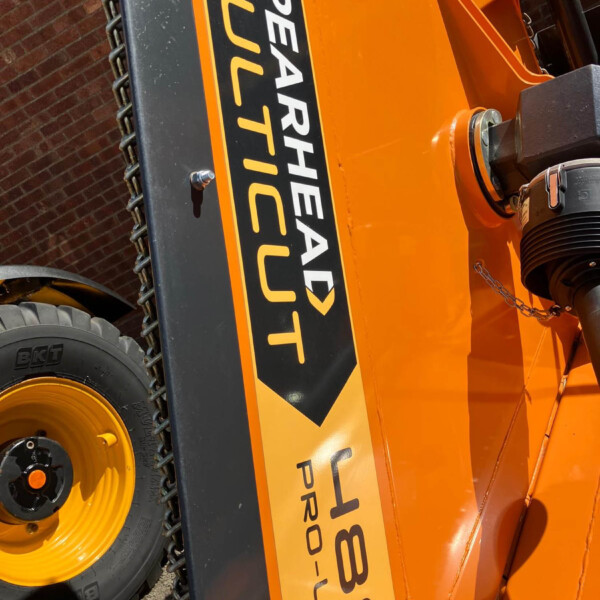 Close-up of an orange heavy-duty construction machine showing a black and yellow warning label, with a chain and hydraulic joint visible on the side.
