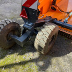Close-up of large rugged tires on an orange heavy equipment vehicle on a gravel surface.
