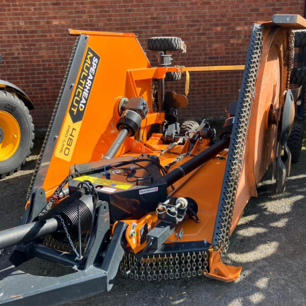 Orange heavy-duty industrial machine with tracks and a chained conveyor, parked against a brick wall.