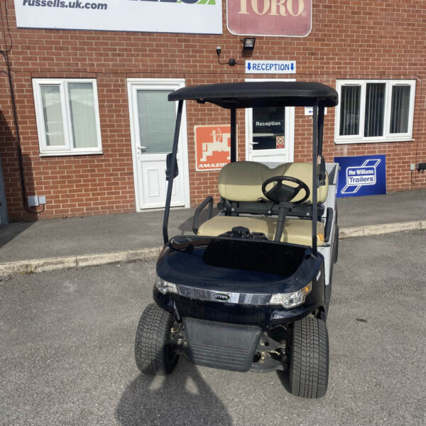 Black golf cart with a beige seat and roof parked in front of a brick building with signs reading RUSSELLS and TORO near a reception door.