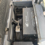 Open battery compartment with a large lithium-ion battery pack labeled 'LITHIUM ION BATTERY PACK' inside an industrial machine. Cables and metal housing visible.