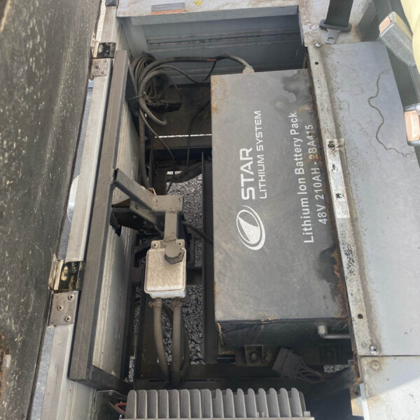 Open battery compartment with a large lithium-ion battery pack labeled 'LITHIUM ION BATTERY PACK' inside an industrial machine. Cables and metal housing visible.
