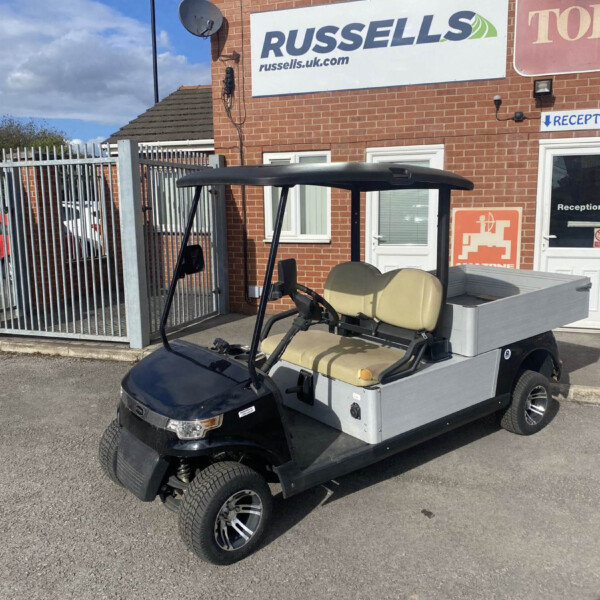 Electric golf cart with beige seats and open cargo area parked in front of a brick building with a Russell's sign.