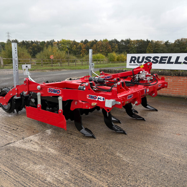 Red agricultural cultivator with blades in a parking area; a Russell's sign is visible in the background.