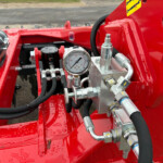 Close-up of red hydraulic machinery showing a pressure gauge, hoses and metal fittings.