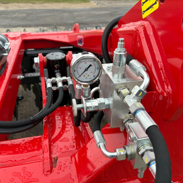 Close-up of red hydraulic machinery showing a pressure gauge, hoses and metal fittings.