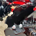 Close-up of black metal brackets and bolts on a red agricultural machinery frame.
