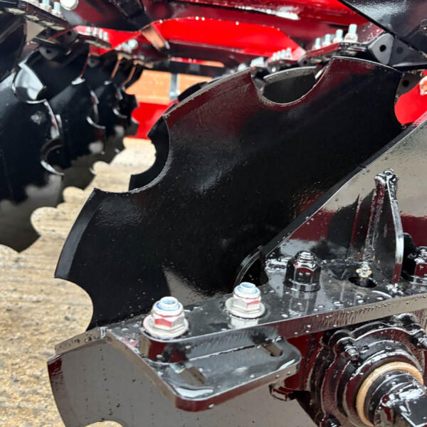 Close-up of black metal brackets and bolts on a red agricultural machinery frame.