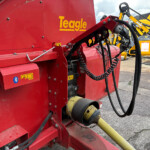 Red Teagle baler with hydraulic hoses and cables, outdoors near yellow machinery in the background.