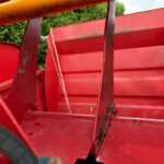 Close-up of red painted metal framework with rust and a white rope, outdoors near greenery.