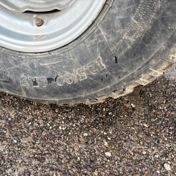 Close-up of a tire mounted on a metal wheel, resting on a gravel driveway.