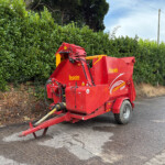 Red Teagle Tomahawk 8500 agricultural machine parked beside a dense green hedge along a street.