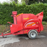 Red Teagle Tomahawk 8500 bale wrapper parked beside a green hedge on a paved surface