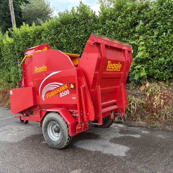 Red Teagle Tomahawk 8500 mower attachment parked on asphalt beside a tall green hedge