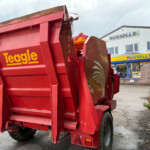 Rear view of a red Teagle bale trailer in a dealership lot with a Russell's storefront in the background.