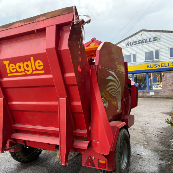 Rear view of a red Teagle bale trailer in a dealership lot with a Russell's storefront in the background.