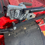 Close-up of a gray lever panel with numbered positions (1, 2) on a red agricultural machine, including a black foam-grip lever and safety stickers nearby.