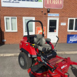 Red Toro Z-Master ride-on lawn mower parked outside a brick building with Russell's and Toro signs visible above.