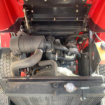 Red truck with hood open, exposing engine components, hoses, and air intake at the front of the engine bay