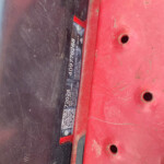 Close-up of a red vehicle frame with a black VIN plate between red and dark panels, showing screws and a small gap between surfaces.