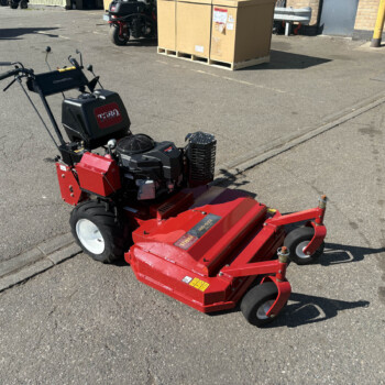 Red Toro riding mower attachment on a cracked asphalt lot with pallets and equipment in the background.