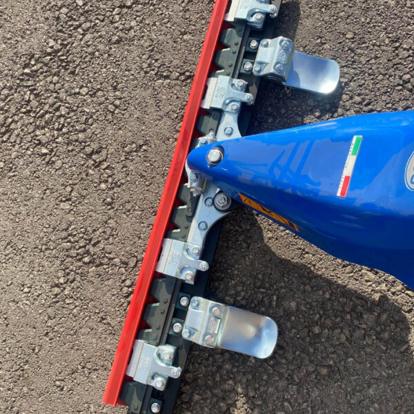Close-up of a blue construction machine with a red cutting edge blade and silver mounting brackets on rough ground.