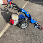 Blue mini motorbike with red handlebars parked by a curb near a trailers sign outside a brick building.