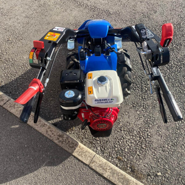 From a rider's viewpoint: blue mini ATV handlebars with red grips and a visible engine, sitting on asphalt beside a curb.