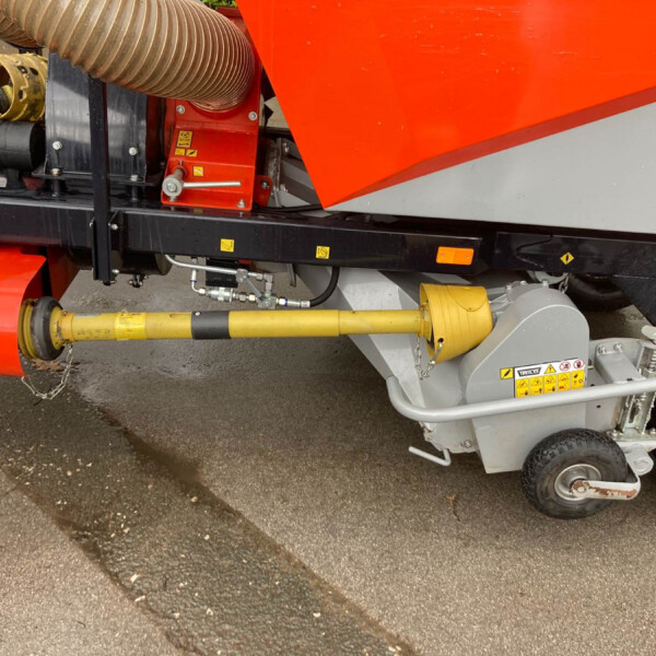 Close-up of orange industrial machinery with a large ribbed hose, yellow pipes, and black frame components.