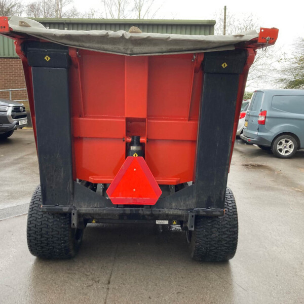 Rear view of a red dump truck trailer in a raised bed position with a grey tarp, parked among cars in a lot.