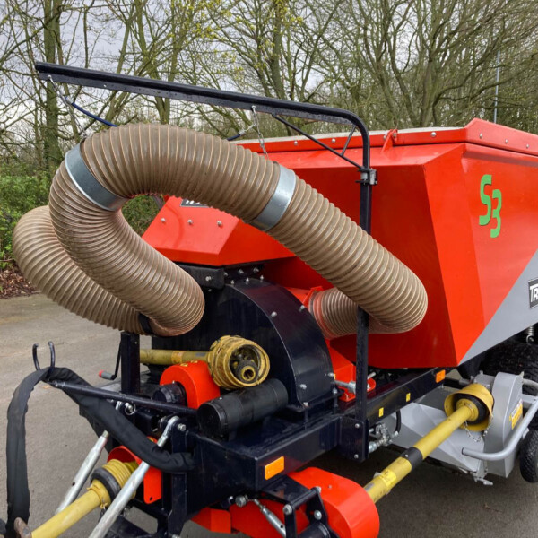 Orange industrial machine with a large beige corrugated hose attached, outdoors near trees and a paved area.