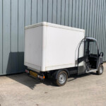 White cargo truck with cab open, parked beside a tall gray corrugated metal wall.