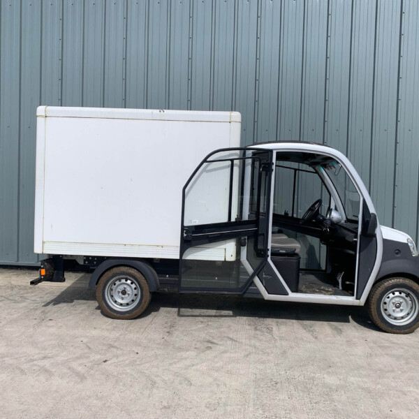 White delivery van with its front passenger door open beside a teal-gray corrugated metal wall.