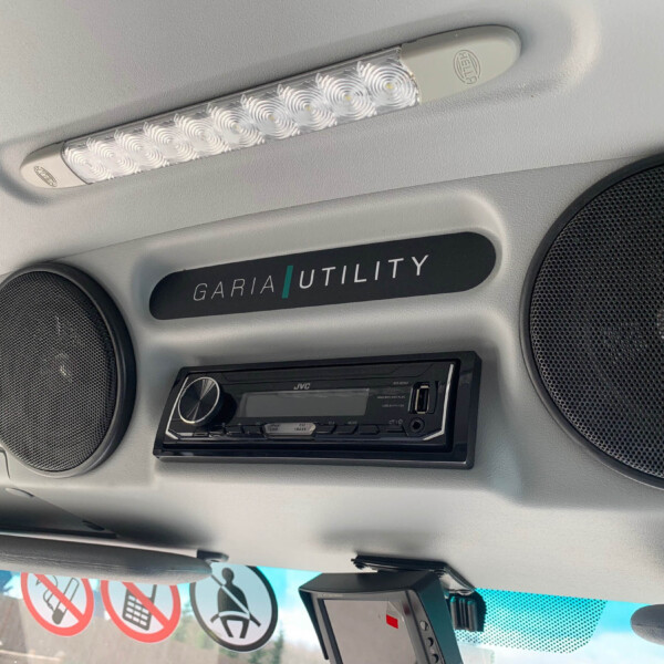 Overhead LED cabin light strip with round speaker grilles on a vehicle’s ceiling.