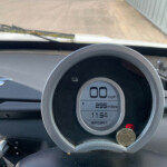 Circular digital car gauge showing 0 mph, 295 miles on the odometer, and time 11:54 in sport mode, with dashboard icons around it.