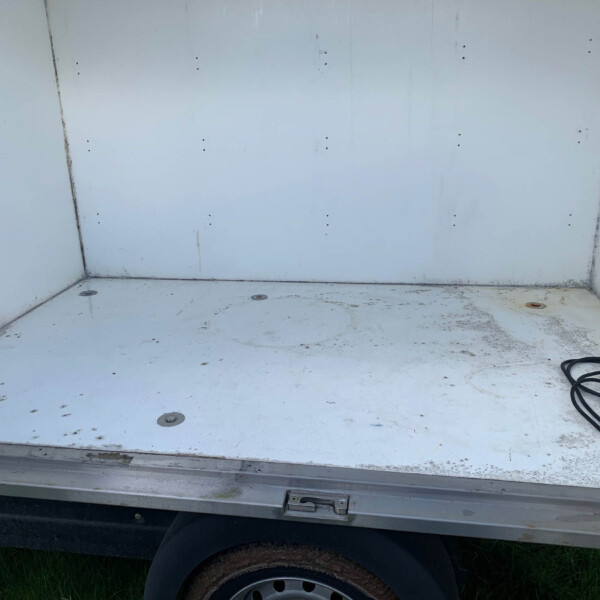 Interior of a dirty white cargo trailer with a coiled black cable on the right side and a dirty, scuffed floor and walls.