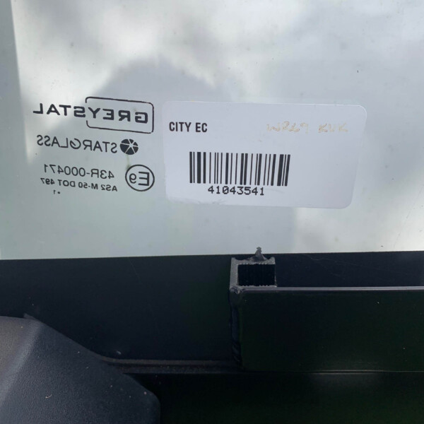 Sticker with a barcode and the text 'CITY EC' on a light metal surface inside a vehicle; label appears partly reversed.