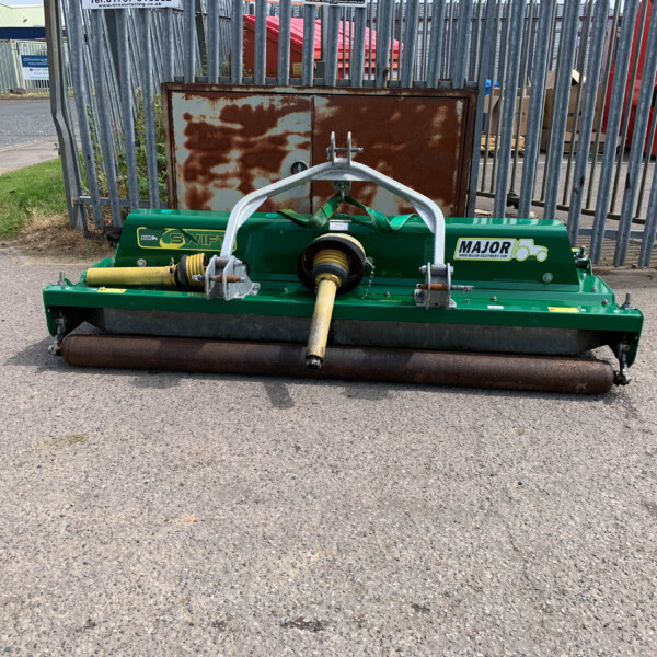 Green Major mower attachment with yellow drive shaft sits in front of a rusty cabinet behind a tall metal fence in an industrial yard.