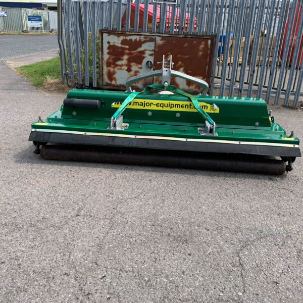 Green street sweeper parked on a paved area in an industrial yard with a rusted metal cabinet and fence in the background.