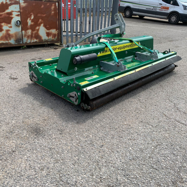 Green street-sweeping machine with a roller brush parked on an asphalt lot, rusted metal cabinet behind.