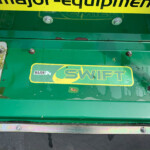 Close-up of a green agricultural machine deck with rust spots, screws, and a bold yellow 'SWIFT' label; small Major Equipment sticker visible on the left.