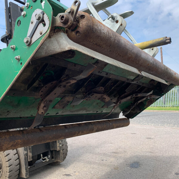 Green agricultural machine underside with a large rusted roller and metal framework under a blue sky