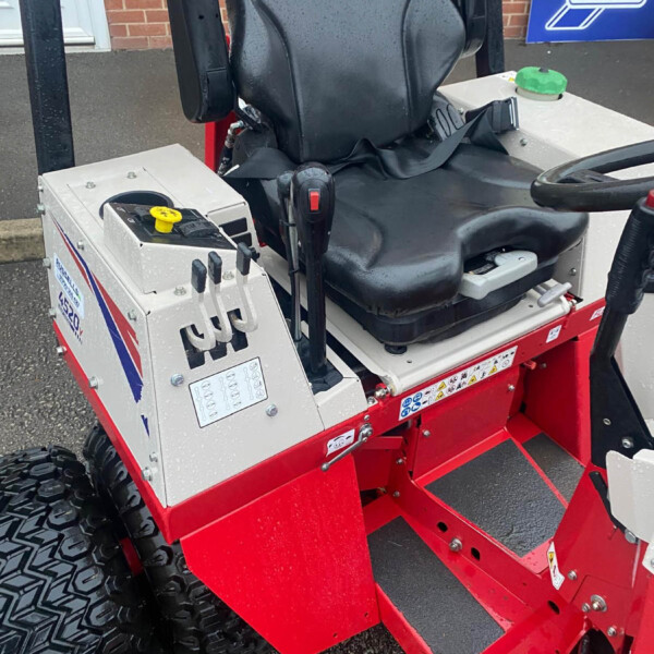 Operator seat and control panel of a red utility vehicle with large knobby tires and a yellow control knob nearby.